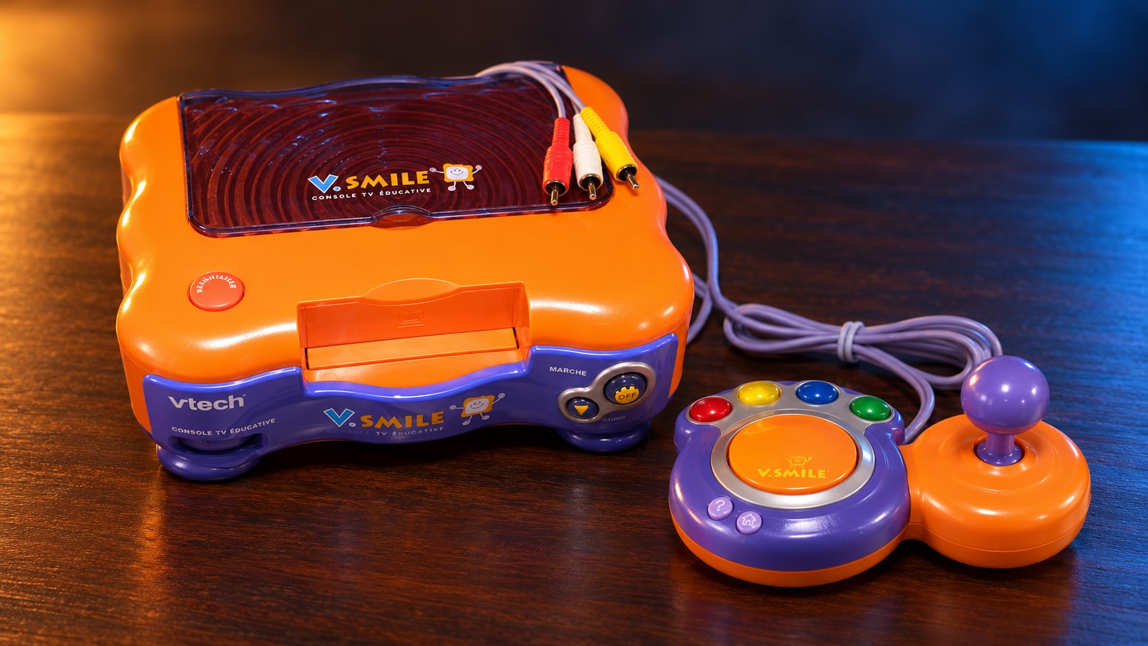 VTech V.Smile mit passendem Controller auf einem dunklen Holztisch vor dezent beleuchtetem Hintergrund